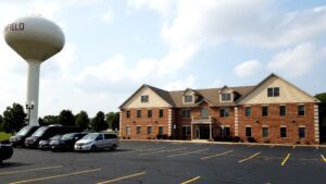 alt=A two-story brick building with multiple windows, containing a custody attorney office building, is located in a parking lot. A large water tower labeled 