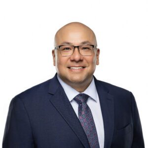 a man in a suit and tie and wearing glasses smiles at the camera, showing the confidence of an experienced divorce lawyer